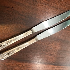 May include: Two silver dinner knives with floral designs on the handles.