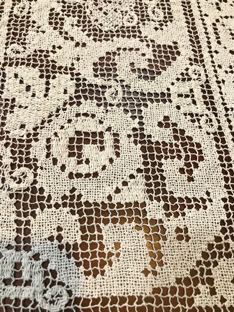 May include: White crocheted lace tablecloth with a delicate floral pattern. The lace is intricate and has a fine texture.