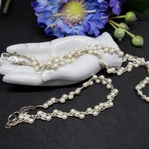 May include: A white pearl necklace with a silver chain. The necklace is displayed on a white ceramic hand.