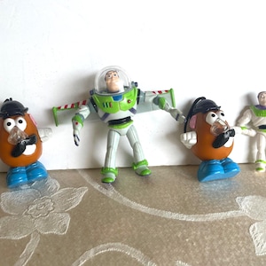 May include: Four Toy Story character figurines. Two Mr. Potato Head figures with black hats and mustaches, a Buzz Lightyear action figure, and a smaller Buzz Lightyear figurine in a white and green spacesuit.