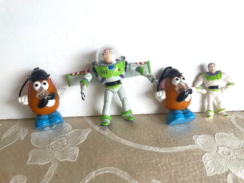May include: Four Toy Story character figurines. Two Mr. Potato Head figures with black hats and mustaches, a Buzz Lightyear action figure, and a smaller Buzz Lightyear figurine in a white and green spacesuit.