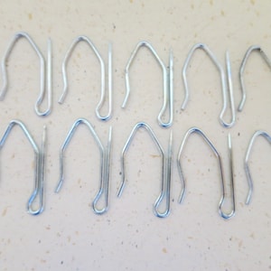 May include: A set of 16 silver curtain hooks. The hooks are made of metal and have a simple design. They are ideal for hanging curtains or drapes.