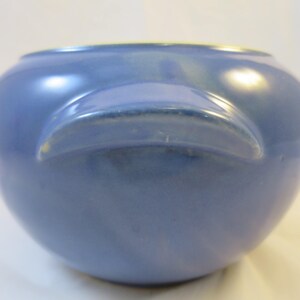 May include: A blue ceramic crock pot with two handles. The crock pot is glazed and has a smooth, rounded shape.