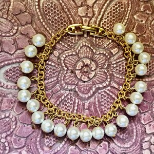 May include: A gold chain bracelet with a clasp closure and white pearl accents. The bracelet has a delicate, feminine design.
