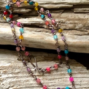 May include: A multi-coloured beaded necklace featuring small, round beads in shades of red, pink, yellow, blue, and purple. The beads are strung on copper wire, and the necklace has a hook clasp.