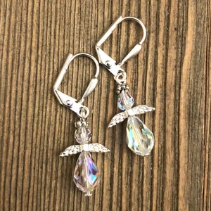 Puede incluir: Un par de pendientes de aro de plata con dijes de &aacute;ngel de cristal. Los &aacute;ngeles tienen alas transparentes y un cuerpo de cristal en forma de l&aacute;grima.