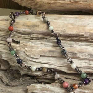 May include: A copper wire wrapped bracelet featuring an assortment of colourful gemstone beads. The beads include amethyst, rose quartz, carnelian, aventurine, and more.