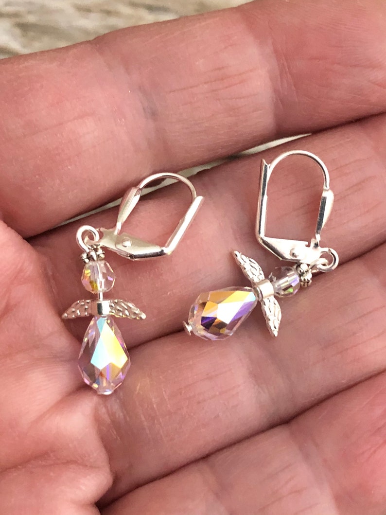 Puede incluir: Un par de pendientes de plata con forma de &aacute;ngel con detalles de cristal iridiscente. Los pendientes presentan un peque&ntilde;o dise&ntilde;o de alas de &aacute;ngel y un cristal en forma de l&aacute;grima.