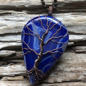 May include: A blue agate pendant with a copper wire tree design. The pendant is on a black chain.