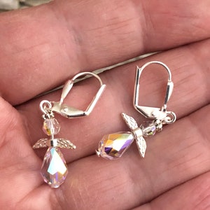 Puede incluir: Un par de pendientes de plata con forma de &aacute;ngel con detalles de cristal iridiscente. Los pendientes tienen un peque&ntilde;o dije de &aacute;ngel con alas y un cristal en forma de l&aacute;grima.