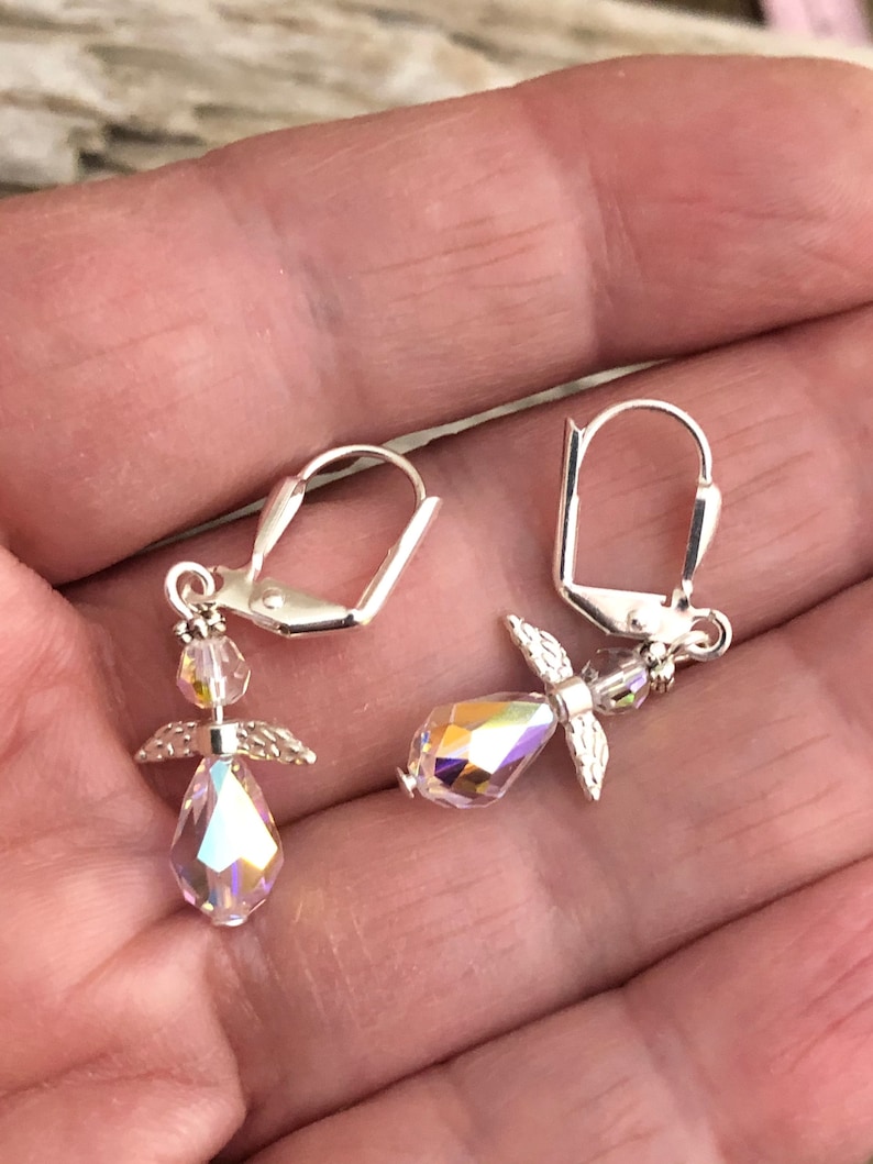 Puede incluir: Un par de pendientes de plata con forma de &aacute;ngel con detalles de cristal iridiscente. Los pendientes tienen un peque&ntilde;o dije de &aacute;ngel con alas y un cristal en forma de l&aacute;grima.