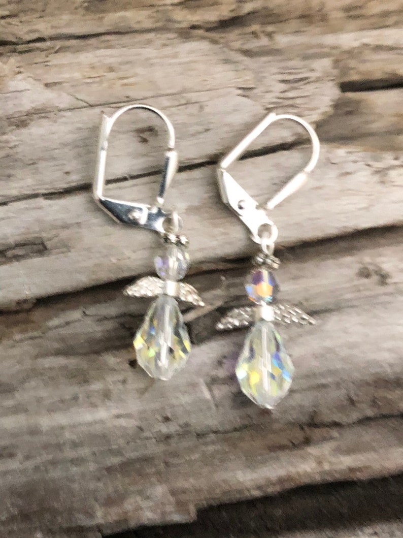 Puede incluir: Un par de pendientes de aro de plata con dijes de &aacute;ngeles de cristal. Los &aacute;ngeles tienen alas transparentes y cuerpos iridiscentes.