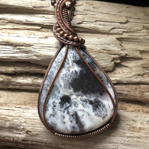 May include: A teardrop-shaped pendant featuring a white and black agate stone wrapped in copper wire. The wire is twisted and beaded, creating a unique and intricate design.