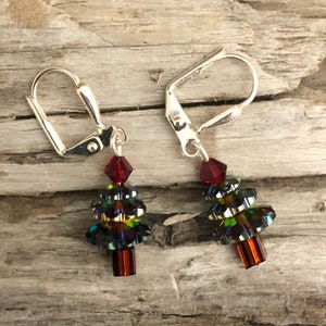 Puede incluir: Un par de pendientes colgantes de plata con un cristal rojo en la parte superior y un diseño de árbol de Navidad de cristal multicolor.