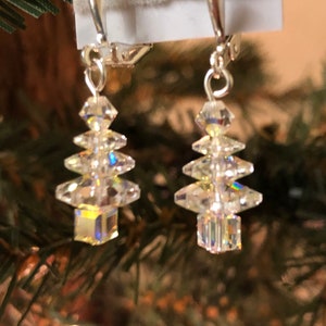 May include: A pair of silver dangle earrings with crystal clear teardrop shaped beads arranged in a Christmas tree shape.