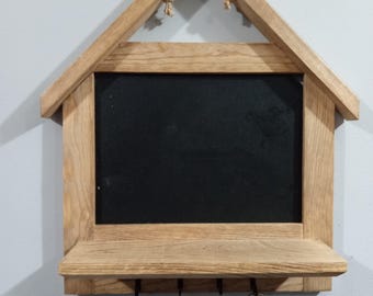 May include: Wooden key holder with a chalkboard and a shelf. The key holder is shaped like a house and has a rope hanger. There are five hooks on the shelf.