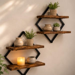 Peut inclure: Deux étagères murales en forme de losange avec des cadres en métal noir et deux planches en bois horizontales chacune. Les étagères supportent diverses petites plantes en pot, des vases en céramique et une bougie allumée.