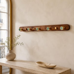 May include: A horizontal wall-mounted coat rack made of dark brown wood featuring four brass hooks with circular green marble-like inlays and three smaller brass accent knobs positioned between the hooks along the length of the wooden board.