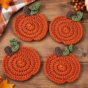 May include: Four round, orange, crocheted pumpkin coasters, each featuring a small brown stem and a green leaf. The coasters are arranged in a square formation, showcasing a textured, circular stitch pattern throughout the pumpkin-shaped design.
