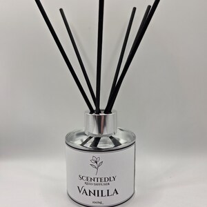 May include: A clear glass reed diffuser with black reeds. The label reads "Scentedly Reed Diffuser Vanilla 100ml". The diffuser has a silver-coloured cap. The reeds are black and extend upwards from the bottle.