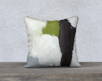 Puede incluir: Cojín cuadrado decorativo con un diseño abstracto. El cojín presenta un fondo blanco con pinceladas verdes, negras y grises. El cojín está sobre una superficie de madera.