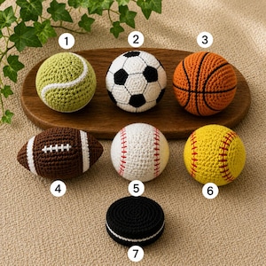 May include: A collection of crocheted sports balls, including a tennis ball, soccer ball, basketball, football, baseball, softball, and hockey puck. The balls are in various colors, such as green, white, orange, brown, yellow, and black. They are arranged on a wooden tray.