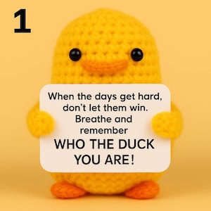 May include: A handmade yellow crochet duck holding a white sign with the text "When the days get hard, don't let them win. Breathe and remember WHO THE DUCK YOU ARE!" The duck has black eyes and an orange beak and feet.