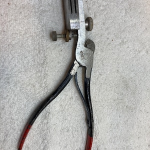 Può includere: Un utensile per set di seghe vintage con una testa in metallo argentato e manici neri con punte rosse. L'utensile ha una vite e una manopola per le regolazioni. L'utensile è progettato per impostare i denti di una lama per sega.