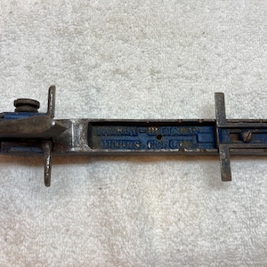 May include: A vintage metal woodworking tool, labelled "Shurley-D. Fixture" and "Tri-uns Co., Ltd.". The tool has a blue painted section and a metal handle with a knob.
