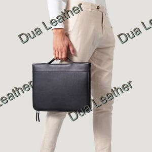 May include: A black leather briefcase with a handle and zipper closure. The briefcase is rectangular and appears to be new. The text "Dua Leather" is visible in the image.