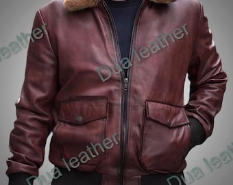May include: A brown leather bomber jacket with a tan shearling collar. The jacket has two front pockets, a zip-up closure, and black ribbed cuffs and hem. The jacket is a classic style.