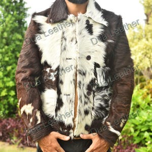 May include: A brown and white cowhide jacket with a classic collar and button closure. The jacket features a unique pattern and a textured appearance, offering a bold and stylish look. The jacket has two pockets and is a statement piece.