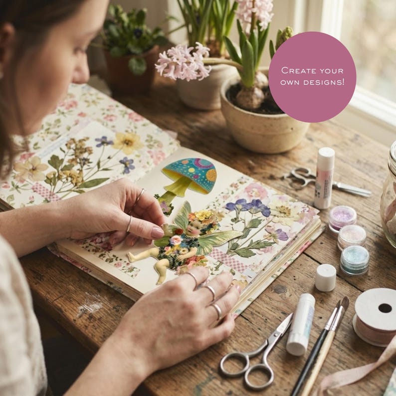 May include: A scrapbook featuring pressed flowers and a fairy illustration with a mushroom, with craft supplies including scissors, glue sticks, and glitter pots on a wooden table. A pink circle contains the text: CREATE YOUR OWN DESIGNS!