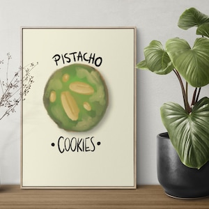 Puede incluir: Impresión enmarcada que presenta una galleta de pistacho verde con trozos de pistacho. El texto "PISTACHO COOKIES" está escrito en negro. Una planta en una maceta negra y un jarrón blanco también están en la imagen.