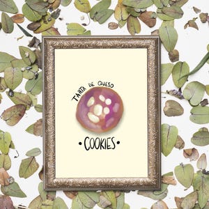 May include: A framed print with a light yellow background, featuring a purple and white illustration of a cookie. The text "Tarta de Queso" and "Cookies" are displayed. The frame is gold, and the background is decorated with green and brown leaves.