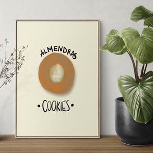 Puede incluir: Impresión enmarcada con una ilustración de galleta de almendras y el texto "ALMENDRAS COOKIES". También se ven un jarrón blanco con ramas secas y una planta en maceta con hojas verdes grandes.
