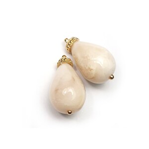 May include: Two white pearlescent teardrop-shaped beads with gold-toned metal caps. The beads have a smooth, glossy finish.