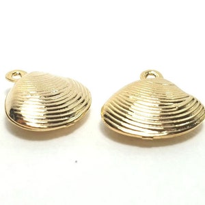 May include: Two gold-coloured seashell charms with a textured surface and a loop at the top for attaching to jewellery. The charms are set against a white background. These charms are ideal for crafting.