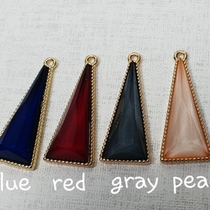 Può includere: Quattro ciondoli a forma di triangolo con bordatura dorata. I ciondoli sono blu, rosso, grigio e pesca.