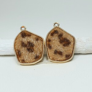 May include: A pair of gold-toned earrings with a leopard print design. The earrings are made of metal and have a textured surface.