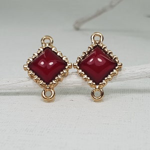 May include: Two gold-tone metal square-shaped pendant charms with a red glass center. Each charm has a loop on the top and two loops on the bottom.