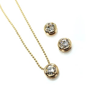 May include: A gold necklace with a round clear crystal pendant and matching earrings. The necklace has a delicate chain.