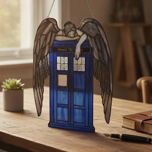 May include: A stained glass suncatcher featuring a blue police box with the text POLICE PUBLIC CALL BOX and a weeping angel figure with large, textured grey wings resting its arms on top of the structure, suspended by a thin metal chain.