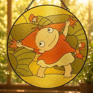 May include: A circular stained glass suncatcher featuring a cartoon character with orange hair wearing a red shirt and white skirt, pulling their hair outward. The background consists of yellow and green glass segments with small orange fish figures.