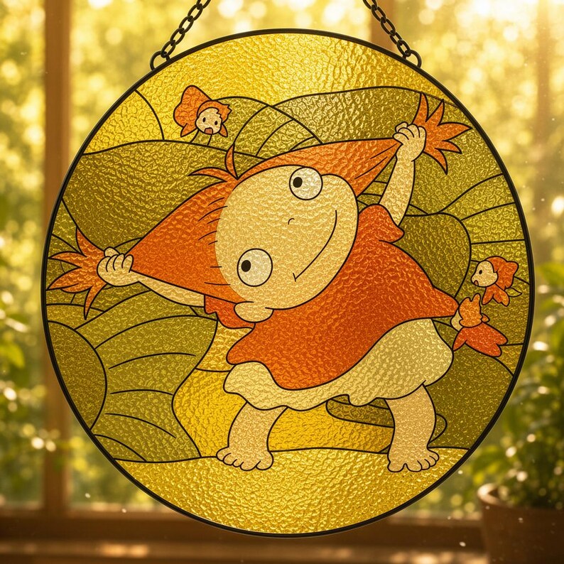 May include: A circular stained glass suncatcher featuring a cartoon character with orange hair wearing a red shirt and white skirt, pulling their hair outward. The background consists of yellow and green glass segments with small orange fish figures.