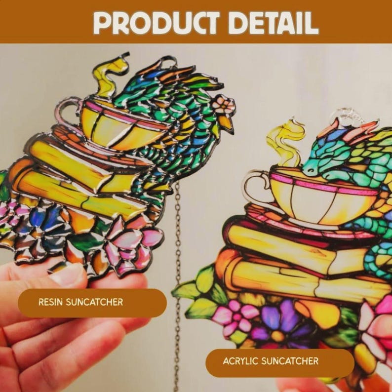 May include: Two suncatchers featuring a dragon resting on a teacup atop a stack of books with flowers at the base. One is labeled RESIN SUNCATCHER and the other ACRYLIC SUNCATCHER. The designs use vibrant colors with black outlines and a hanging chain.