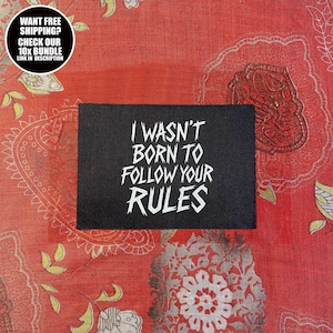 May include: A black rectangular patch with the white text "I WASN'T BORN TO FOLLOW YOUR RULES." The patch is set against a red patterned background. A circular graphic in the upper left corner reads "WANT FREE SHIPPING? CHECK OUR 10x BUNDLE LINK IN DESCRIPTION."