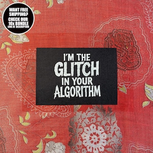 May include: A black rectangular patch with the text "I'M THE GLITCH IN YOUR ALGORITHM" in white. The patch is set against a red patterned fabric. A circular graphic in the upper left corner reads "WANT FREE SHIPPING? CHECK OUR 10X BUNDLE LINK IN DESCRIPTION."