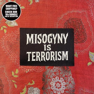 以下が含まれることがあります： 黒い長方形のパッチ。白いゴシック様式の文字で「MISOGYNY IS TERRORISM」と書かれています。パッチは赤い模様の生地に配置されています。左上隅の円形グラフィックにはテキストが含まれています。