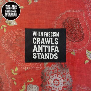 May include: A black patch with white text reading "WHEN FASCISM CRAWLS ANTIFA STANDS" is set against a red patterned backdrop. A circular graphic in the top left corner states "WANT FREE SHIPPING? CHECK OUR 10X BUNDLE LINK IN DESCRIPTION."